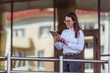 © Volha - Portrait of smiling business woman using tablet pc in front of office building.