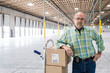 © Mint Images - Portrait of senior man standing with hand truck in warehouse