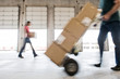 © Mint Images - Man pushing hand truck loaded with cardboard box in warehouse