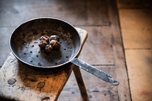 Close Up Of Frying Pan With Roasted Chestnuts On Rustic Wooden Table