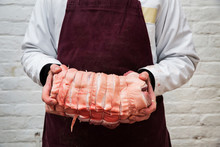 Close Up Of Butcher Wearing Apron Holding Large Rolled Pork Belly