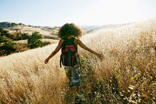 Rear View Of Young Woman With Backpack Hiking In Field