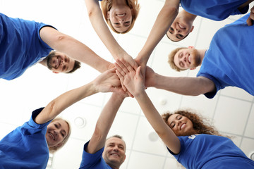 Wall Mural - Team of volunteers putting their hands together on light background, bottom view