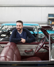 Portrait Of Man Leaning On Classic Convertible Car In Automobile Repair Shop