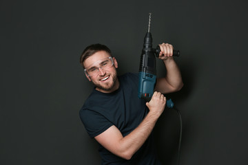 Wall Mural - Young working man with rotary hammer on dark background