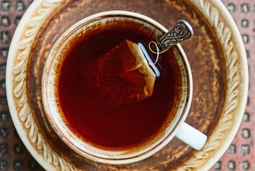 red tea in a cup with a bag and spoon on a saucer