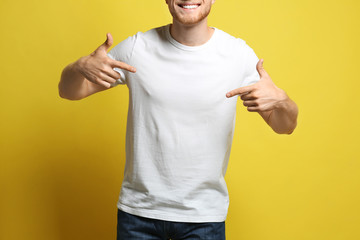 Wall Mural - Young man wearing blank t-shirt on yellow background, closeup. Mockup for design