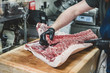 © Mint Images - Midsection of man cutting pork ribs on butcher's block