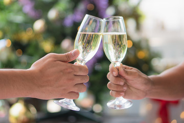 cheerfuls Friends toasting sparkling wine. Close-ups hands of two friends toasting wine glass in the dinner party for celebrating new year on the bokeh of light decorate on christmas tree background.