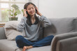 © Pormezz - Relaxed asian woman in headphones listening music on the sofa.