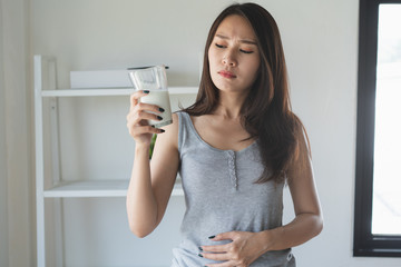 lactose intolerance concept. Woman holding a glass of milk and having a stomachache.