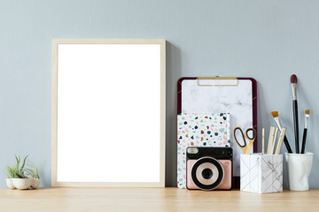 Home interior with mock up photo frame on the brown wooden table with office accesories, instant camera, air plant in design pots, notebook and notes. Grey walls. Minimal concept of mockup. Template.