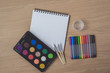 © nipastock - Notepad or notebook with Many colorful pens, paintbrush and Watercolor palette on brown wood table.using for Arts and Education background