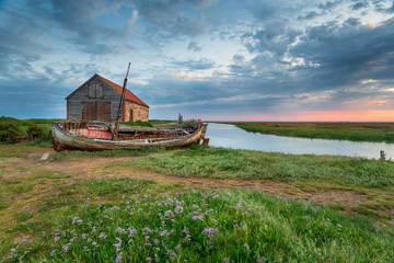 Wall Mural - Summer sunrise over an old coal barn and fishing boat at Thornham on the north coast of Norfolk