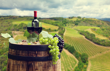 Red wine bottle and wine glass on wodden barrel. Beautiful Tuscany background