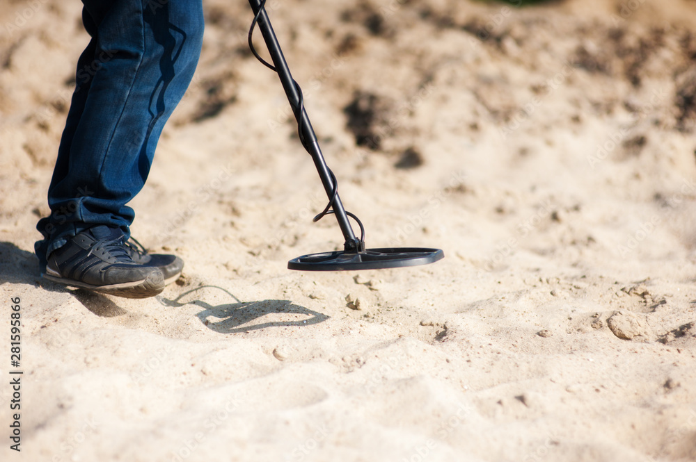 A man is looking in the sand with a metal detector - obrazy, fototapety, plakaty 