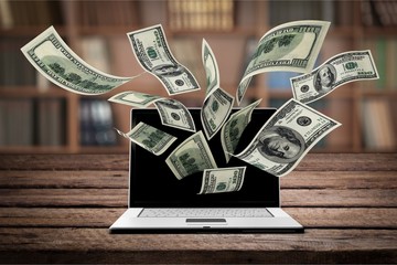 Canvas Print - Finance and earning concept, one hundred dollar banknotes flying around laptop, internet, side view on dark background.