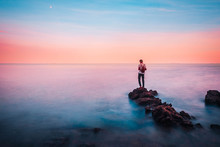 Young Man Stand On A Rock In The Foreground Of Him Have The Sea And Sky Brightly Colored Look Like A Dream In Heaven.