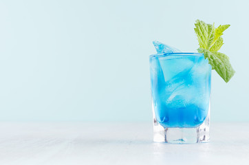 Exquisite blue cocktail for celebration in beach style with blue curacao, ice cube, green mint in mint color bar interior on white wood table.