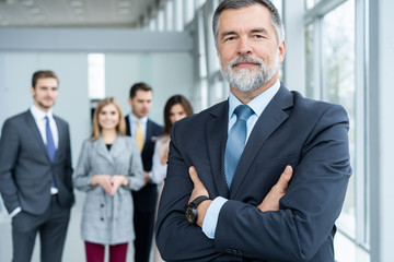 Businessteam in office, Happy Senior Businessman in His Office is standing in front of their team.