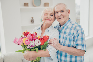 Photo of two adorable aged people hugging pair anniversary holiday surprise big red tulips bunch flat indoors