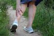 Foot pain, ankle sprain, woman grabbed her leg while walking on a green grass. Concept of tired legs, injury on running