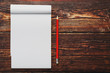 © Alexander - Notebook with a red pencil on a brown background with warm sunlight, for writing. Free empty space for writing on a blank sheet of a notebook.