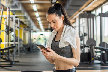 Wall Mural - Young sportive woman using phone after training in gym