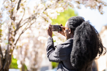 Wall Mural - Rear view of african american tourist woman visiting a picturesque city street destination, using a smart phone taking pictures on summer holiday, outdoors. Black woman travel technology recreation.