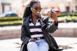 © F8  \ Suport Ukraine - Cheerful african tudent girl talking at video call with smartphone in the street