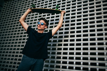 Wall Mural - Young boy in glasses posing with a longboard. street photo, life style