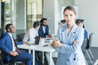© xartproduction - Business woman stands on the background of partners. A team of young businessmen working and communicating together in an office. Corporate businessteam and manager in a meeting