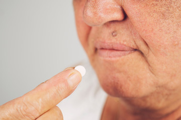 Mature senior middle aged woman holding pill taking painkiller to relieve pain, medicine supplements vitamins, antibiotic medication, meds for old person concept, close up view