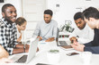 © xartproduction - A team of young office workers, businessmen with laptop working at the table, communicating together in an office. Corporate businessteam and manager in a meeting. coworking.