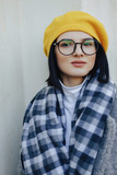 Fototapeta  - Attractive young girl in glasses in coat and yellow Beret on a simple light background