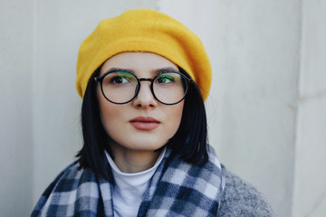 Wall Mural - Attractive young girl in glasses in coat and yellow Beret on a simple light background