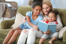 Happy Woman With Her African-American Daughters Reading Book At Home