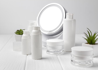 Cosmetic bottle containers with herbs and mirror on wooden table.