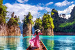 © tawatchai1990 - Beautiful girl standing on the boat and looking to mountains in Ratchaprapha Dam at Khao Sok National Park, Surat Thani Province, Thailand.