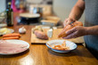 Mann und Hobbykoch schält Süsskartoffel in der Küche, Fisch Filet und viele Zutaten auf Holz Arbeitsplatte