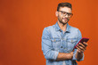 Great news! Happy young man in glasses typing sms isolated against orange background.
