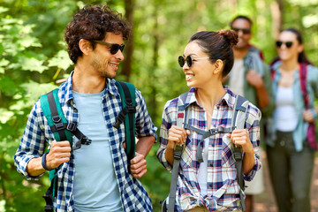 Wall Mural - travel, tourism, hike and people concept - group of friends walking with backpacks in forest