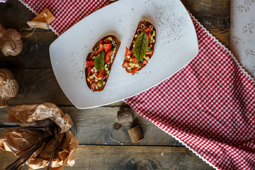 two bruschettes with tomato and cucumber and green leaf on a white plate on a Board table