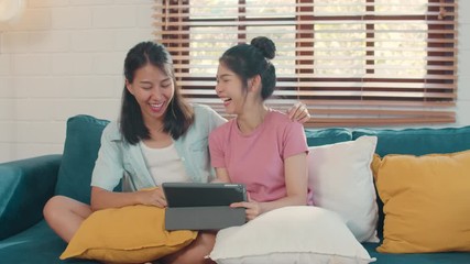 Wall Mural - Young Lesbian lgbtq Asian women couple using tablet at home. Asian lover female happy relax fun using technology watching movie in internet together while lying sofa in living room concept.