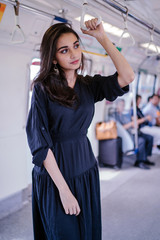 Wall Mural - Portrait of a tall, slim, elegant, attractive, slim and beautiful Indian Asian woman taking the train alone. She is smiling as she holds onto the handrails.