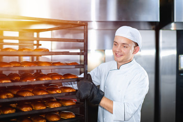 baker takes out a trolley pin for baking trays from a hot industrial oven.