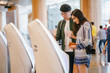 © Danon - A portrait of a pair of young and excited Asian travelers (Korean man and his Indian friend) checking in to board their plane for their holiday at an automated check-in booth in the airport.