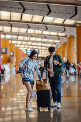 Wall Mural - A young interracial diverse couple (a Korean man and Indian woman) casually dressed as they check their luggage in the middle of an airport during the day. 