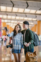 Wall Mural - A young and diverse Asian couple (Korean man and his Indian girlfriend) take a selfie together in a new country. They have just arrived in a new country for a tour and are excited.