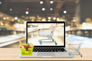 Wall Mural - supermarket aisle blurred background with laptop computer and shopping cart on wood table grocery online concept